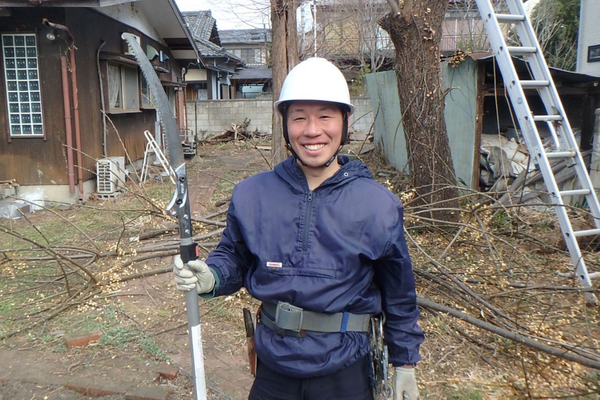 安村さん。写真の後ろに写る2本の木の切り倒しをお願いしました。